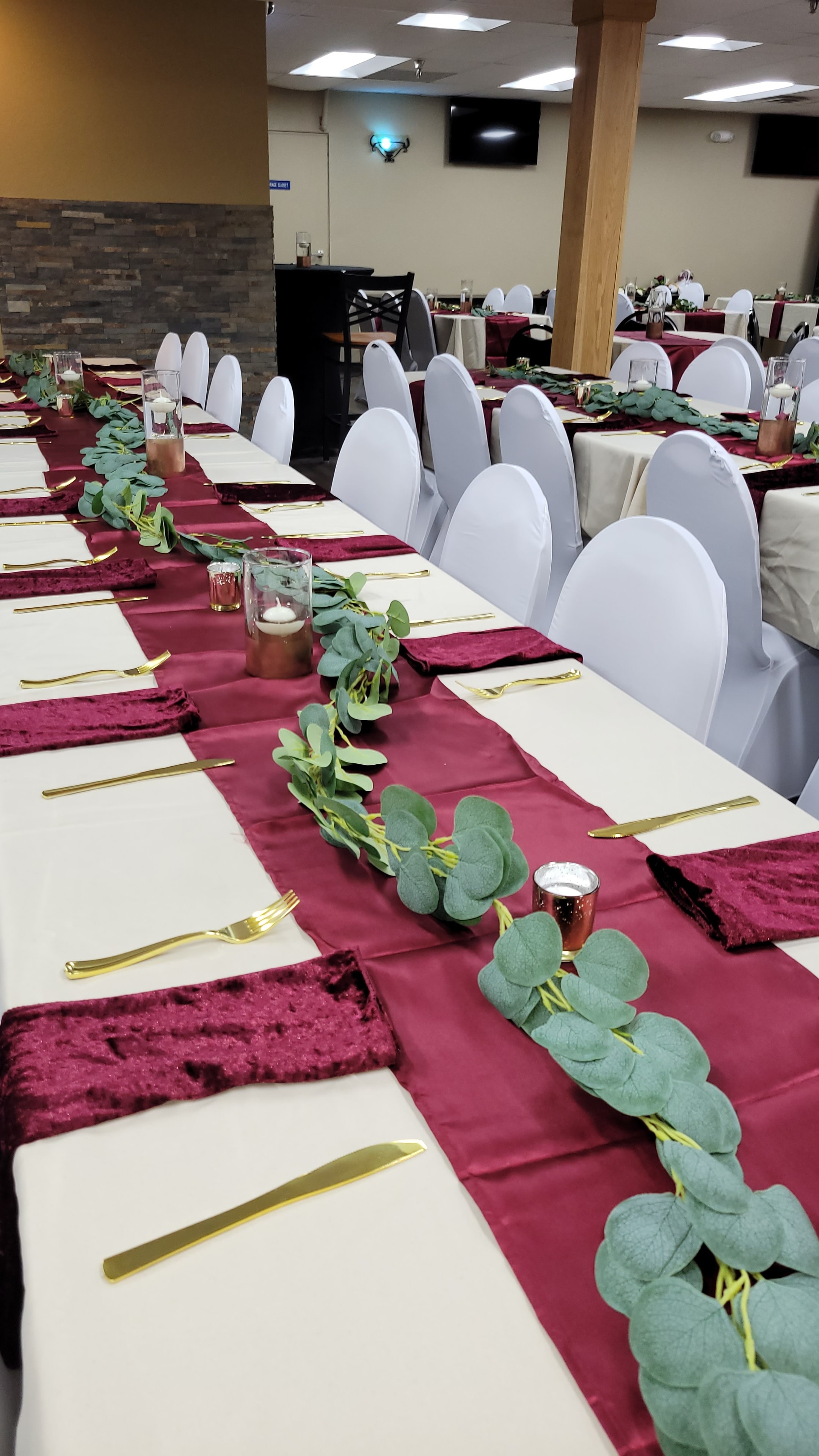 Burgundy corporate table setting with greenery, candles, and gold flatware