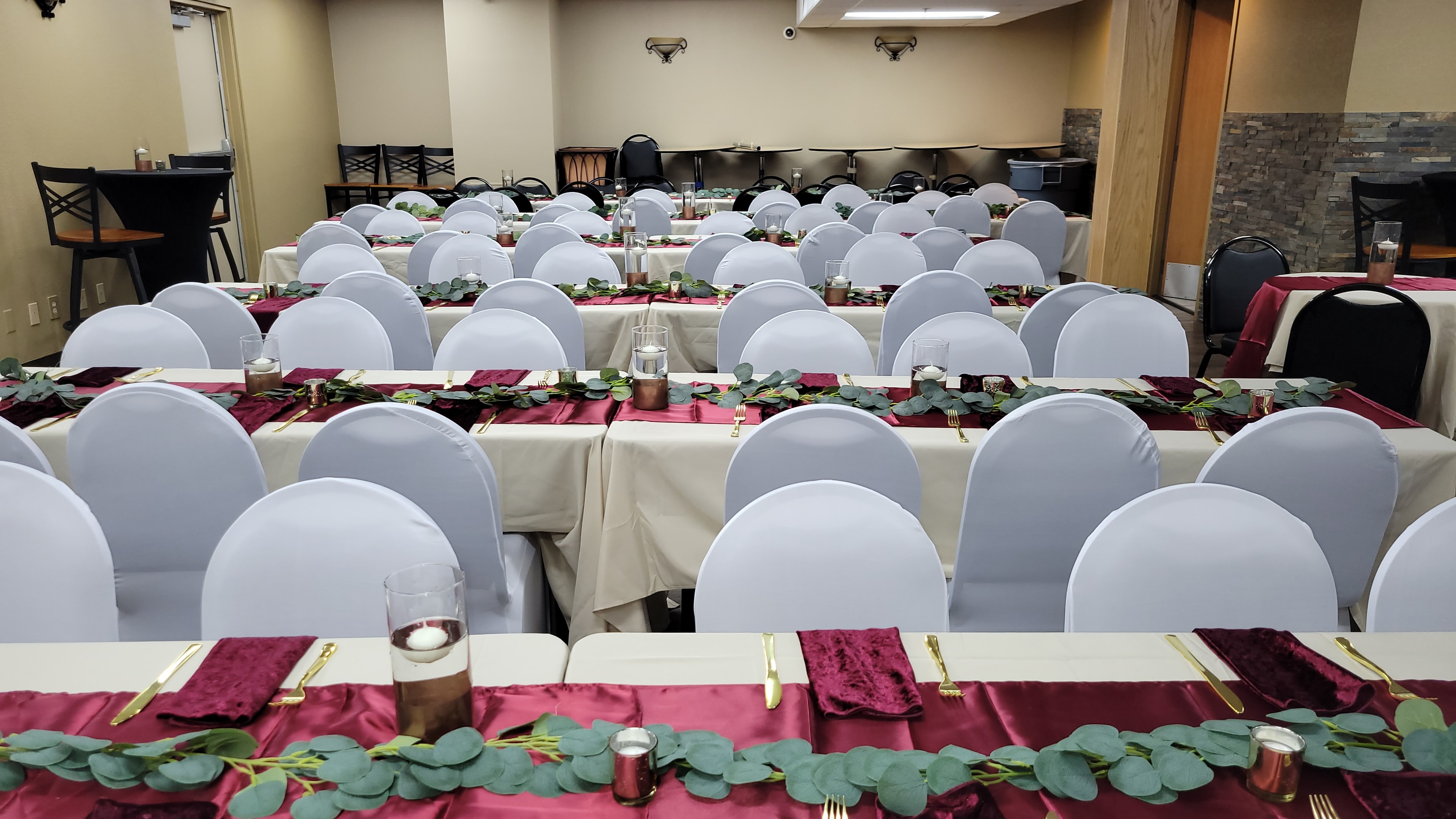 Corporate event tables with burgundy runners, greenery, and white chair covers